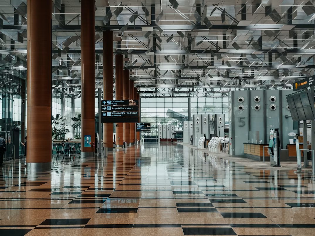 An airport terminal check-in hall with wood-clad columns, self-service kiosks and flight information displays